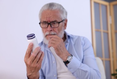 Photo of Senior man with bottle of pills at home, selective focus