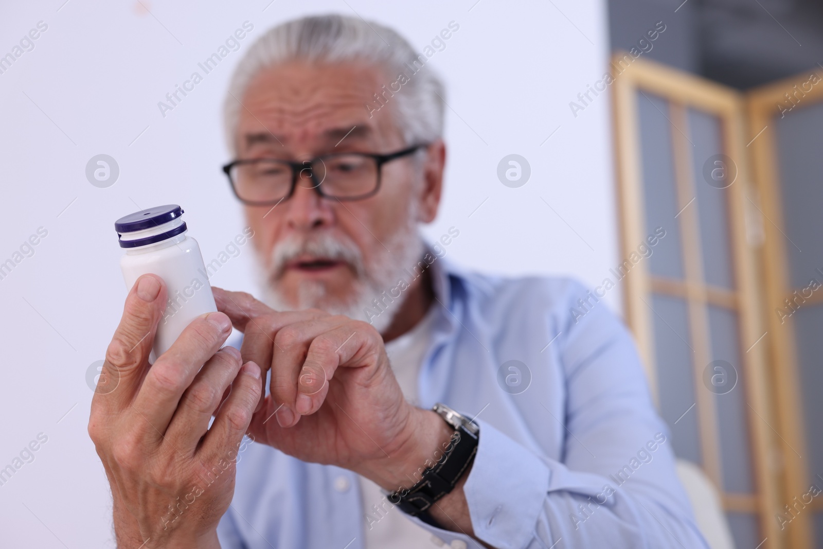 Photo of Senior man with bottle of pills at home, selective focus