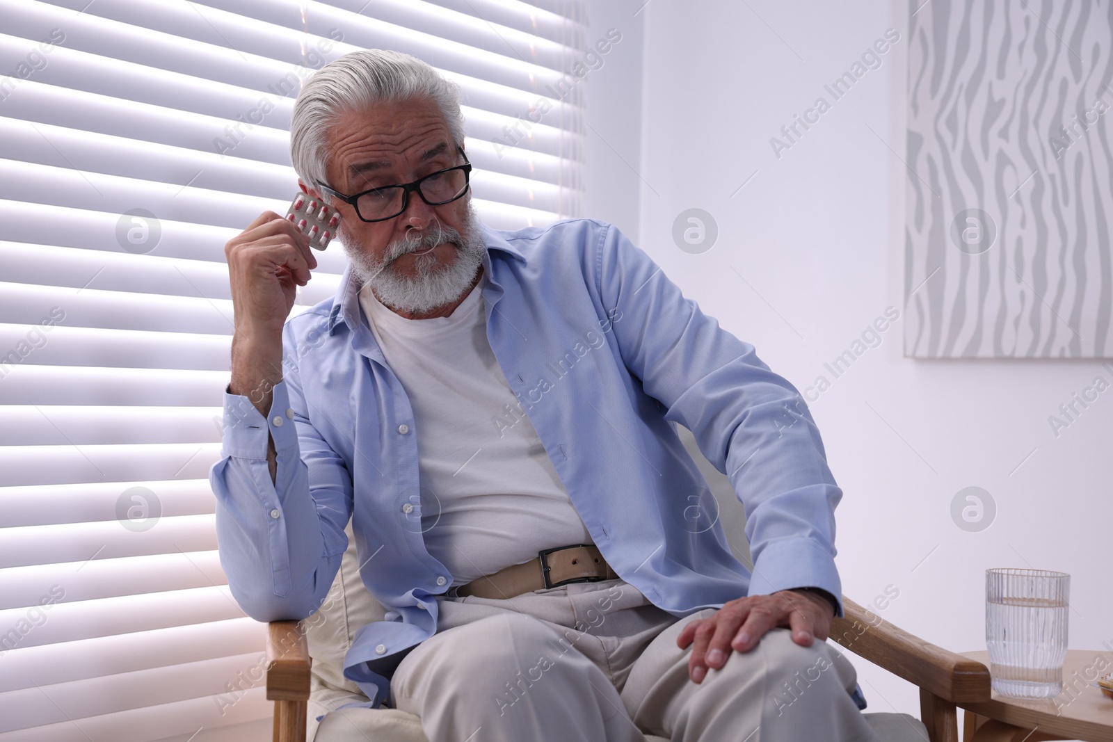 Photo of Senior man holding blister with pills at home