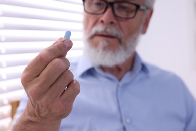 Senior man with pill at home, selective focus