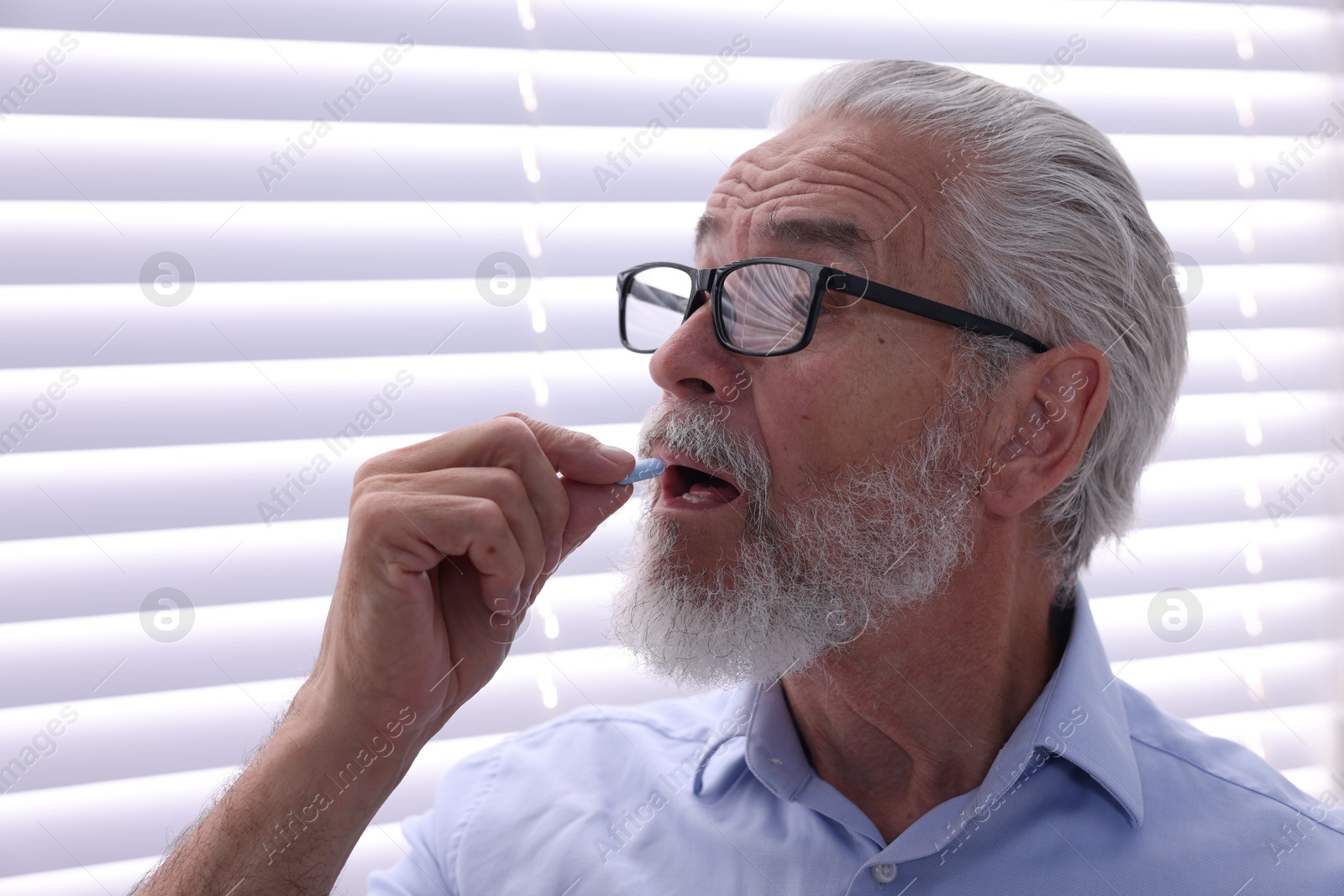 Photo of Senior man in glasses taking pill at home