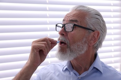 Photo of Senior man in glasses taking pill at home