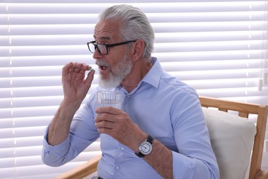 Senior man with glass of water taking pill at home