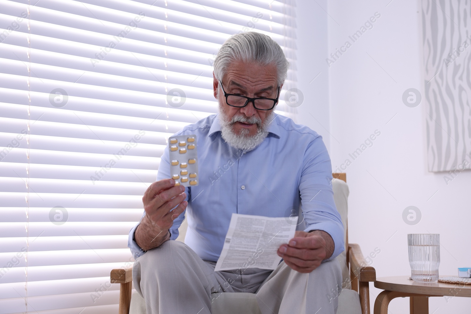 Photo of Senior man with pills reading medicine instruction at home