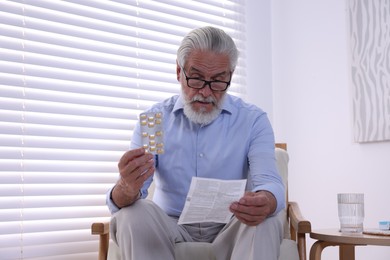 Senior man with pills reading medicine instruction at home