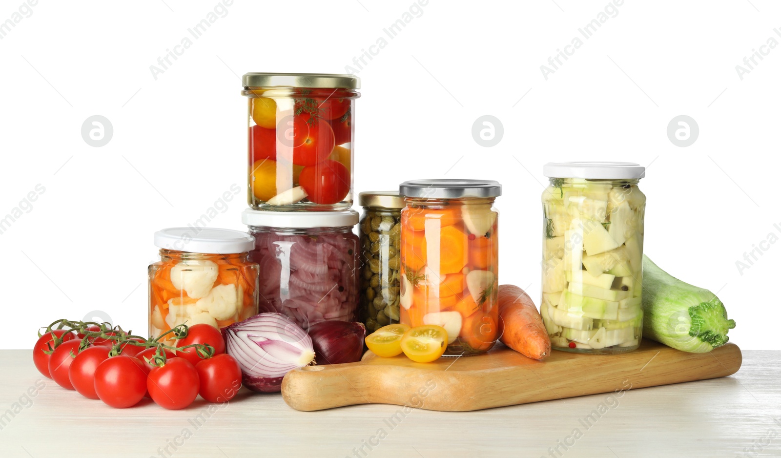 Photo of Different pickled products in jars and fresh vegetables on light wooden table against white background