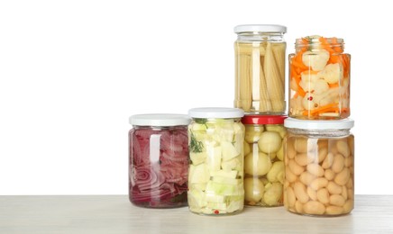 Photo of Different pickled products in jars on light wooden table against white background