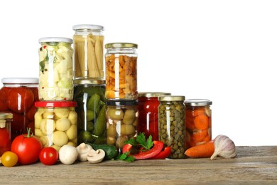 Different pickled products in jars and fresh vegetables on wooden table against white background