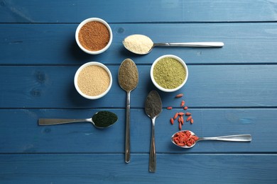 Different superfood powders on blue wooden table, flat lay