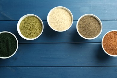 Photo of Different superfood powders in bowls on blue wooden table, flat lay