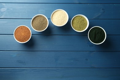 Different superfood powders in bowls on blue wooden table, flat lay. Space for text