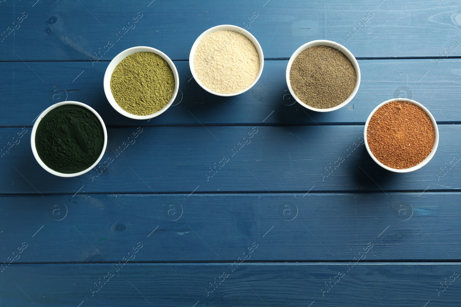 Photo of Different superfood powders in bowls on blue wooden table, flat lay. Space for text