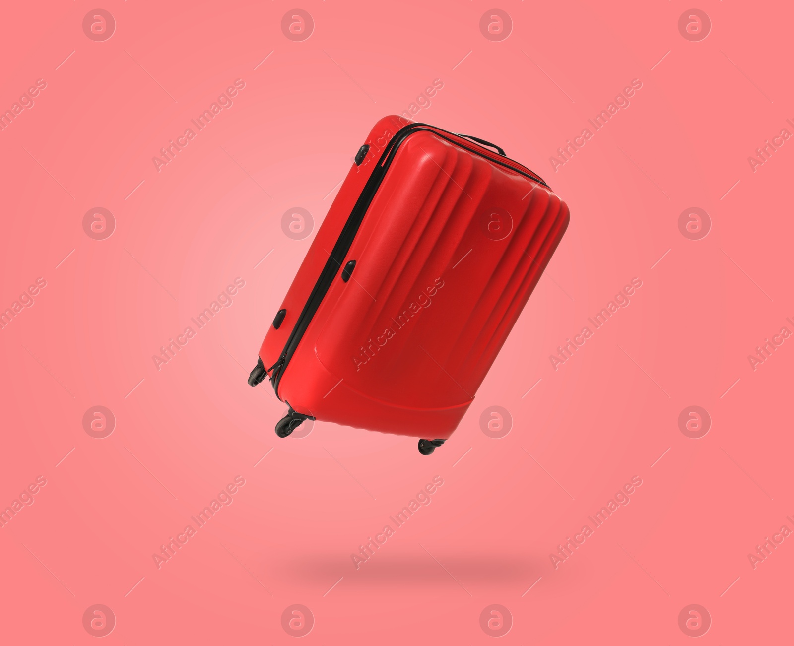 Image of Red suitcase in air on coral background