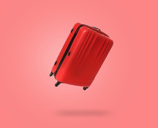 Image of Red suitcase in air on coral background