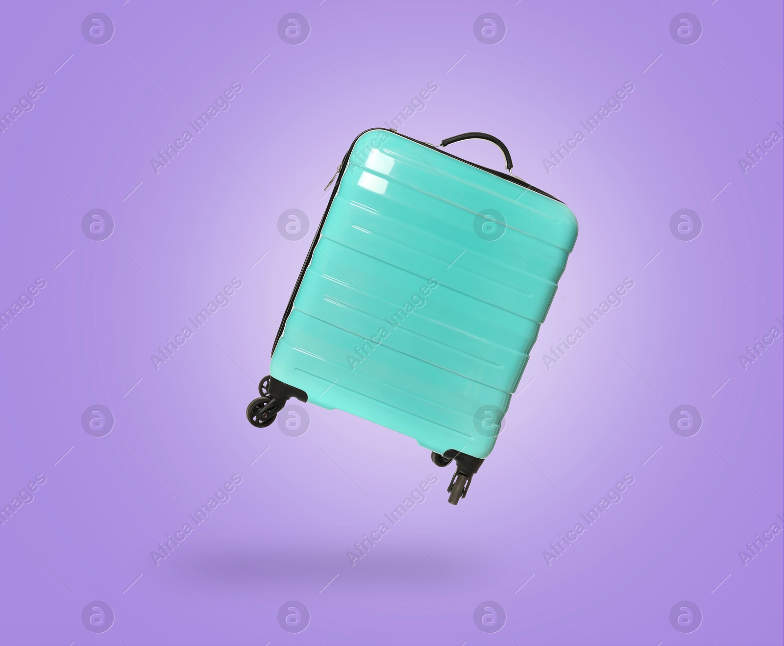 Image of Turquoise suitcase in air on violet background