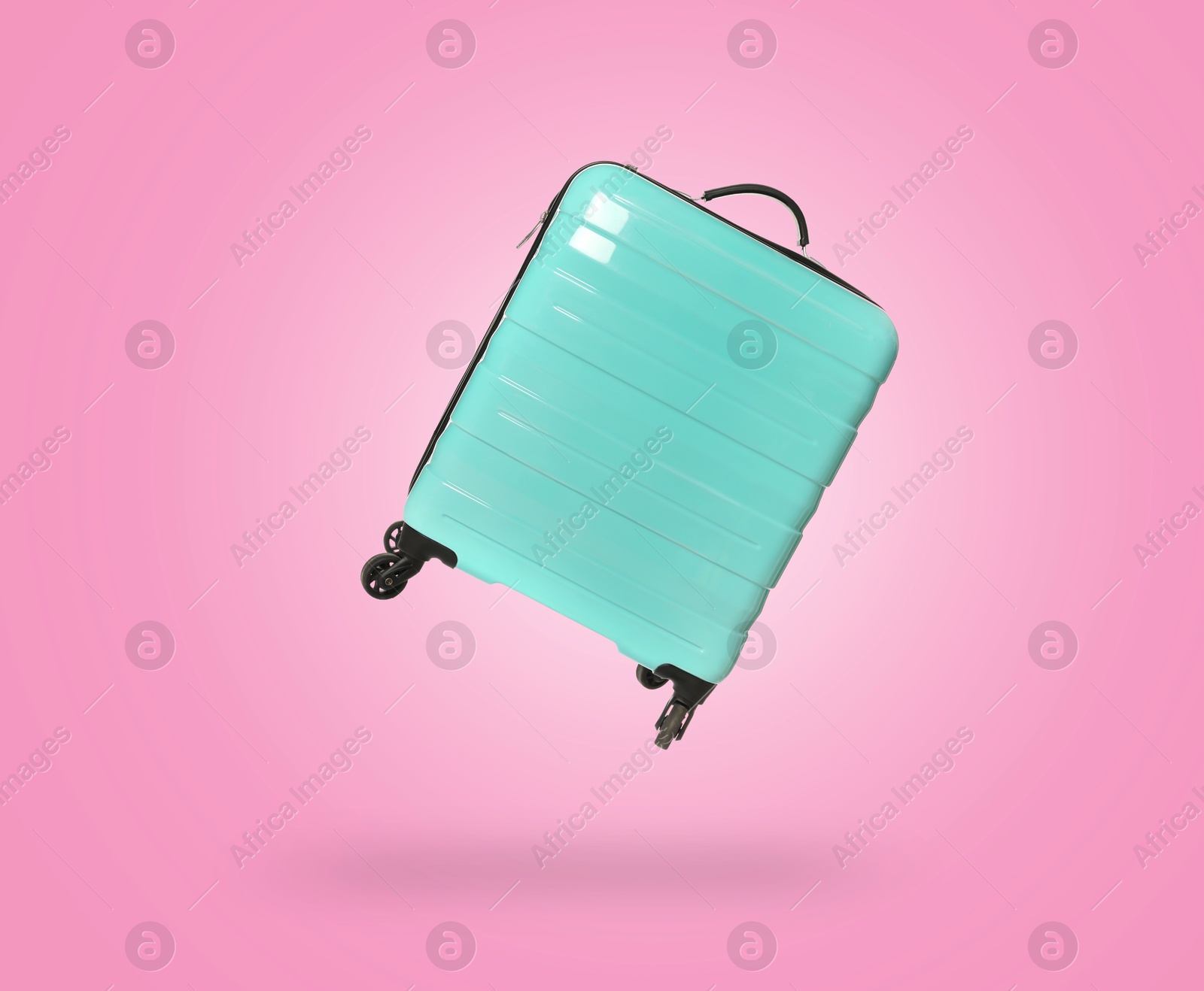 Image of Turquoise suitcase in air on pink background