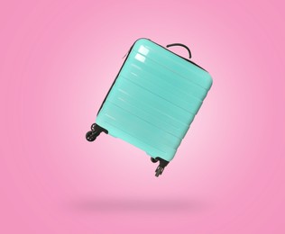 Image of Turquoise suitcase in air on pink background