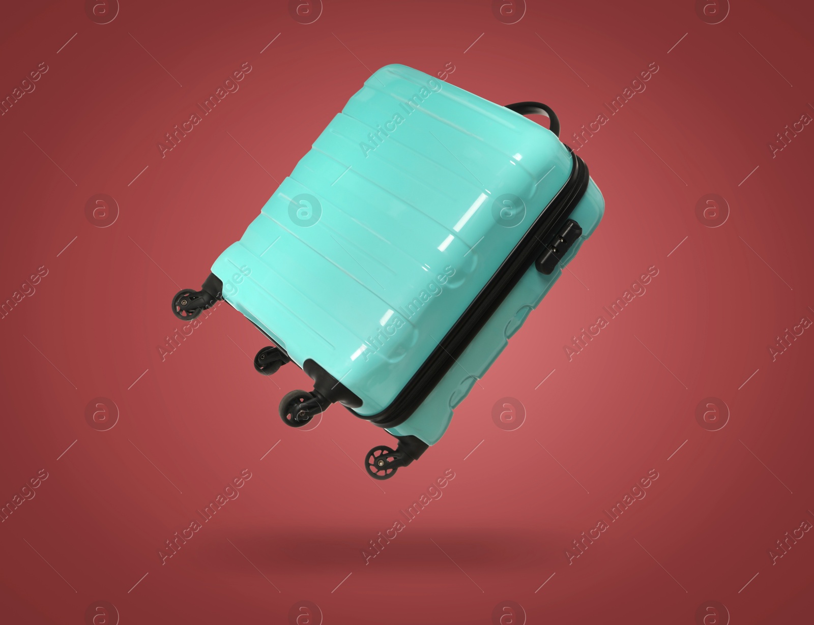 Image of Turquoise suitcase in air on burgundy background