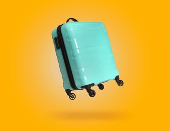 Image of Turquoise suitcase in air on orange background