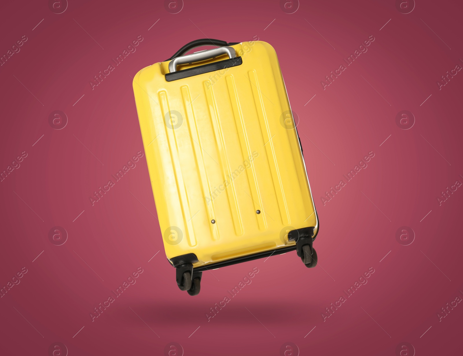 Image of Yellow suitcase in air on burgundy background