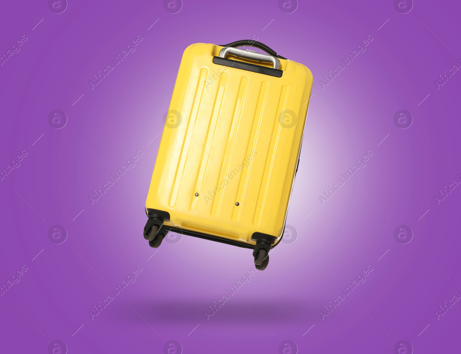 Image of Yellow suitcase in air on dark violet background