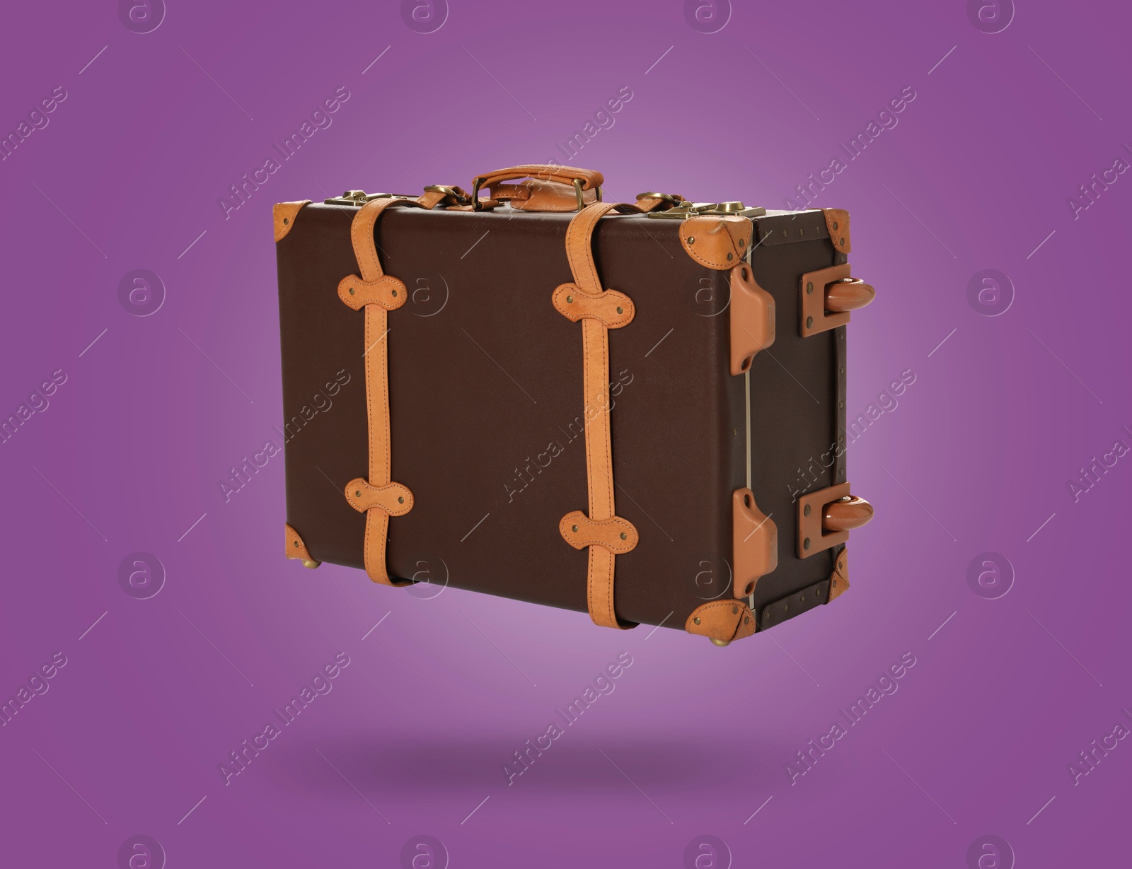 Image of Vintage suitcase in air on purple background