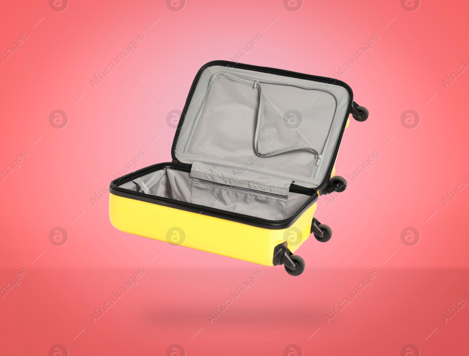 Image of Open empty suitcase in air on coral background