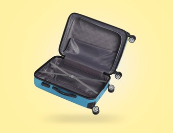 Image of Open empty suitcase in air on pale yellow background