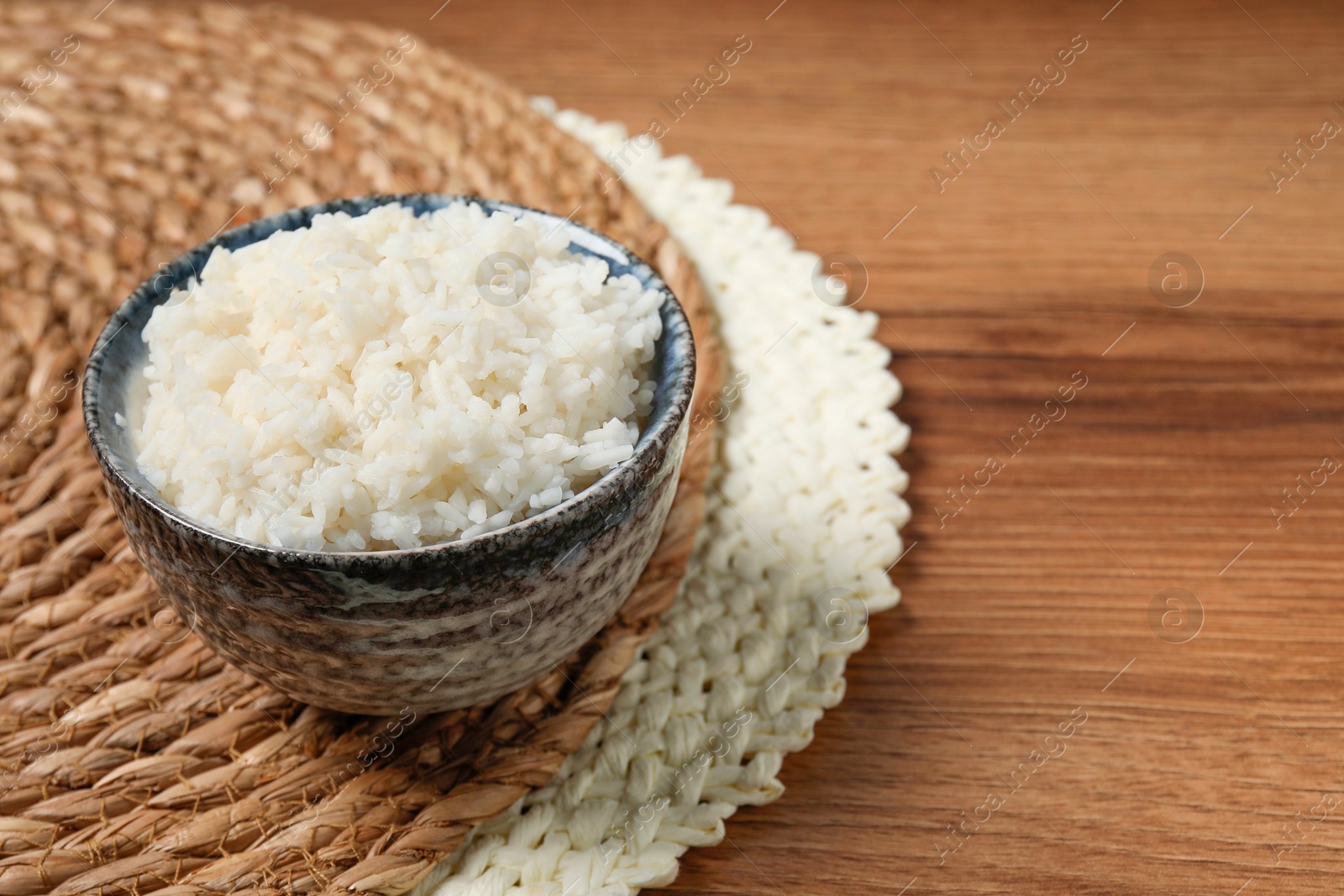 Photo of Tasty cooked rice in bowl on wooden table, space for text