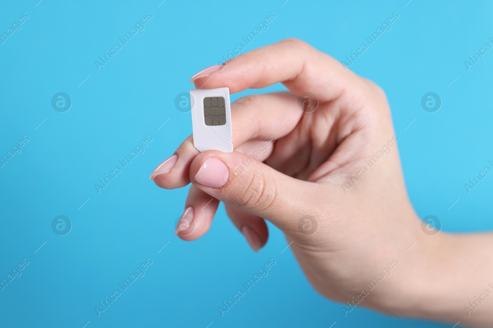 Photo of Woman holding SIM card on light blue background, closeup