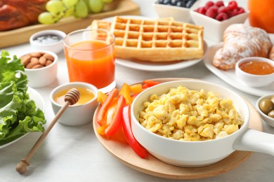 Tasty breakfast. Scrambled eggs in bowl, bell pepper and other food on light table, closeup