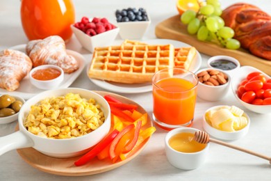 Photo of Tasty breakfast. Scrambled eggs in bowl, bell pepper, honey and other food on light table, closeup