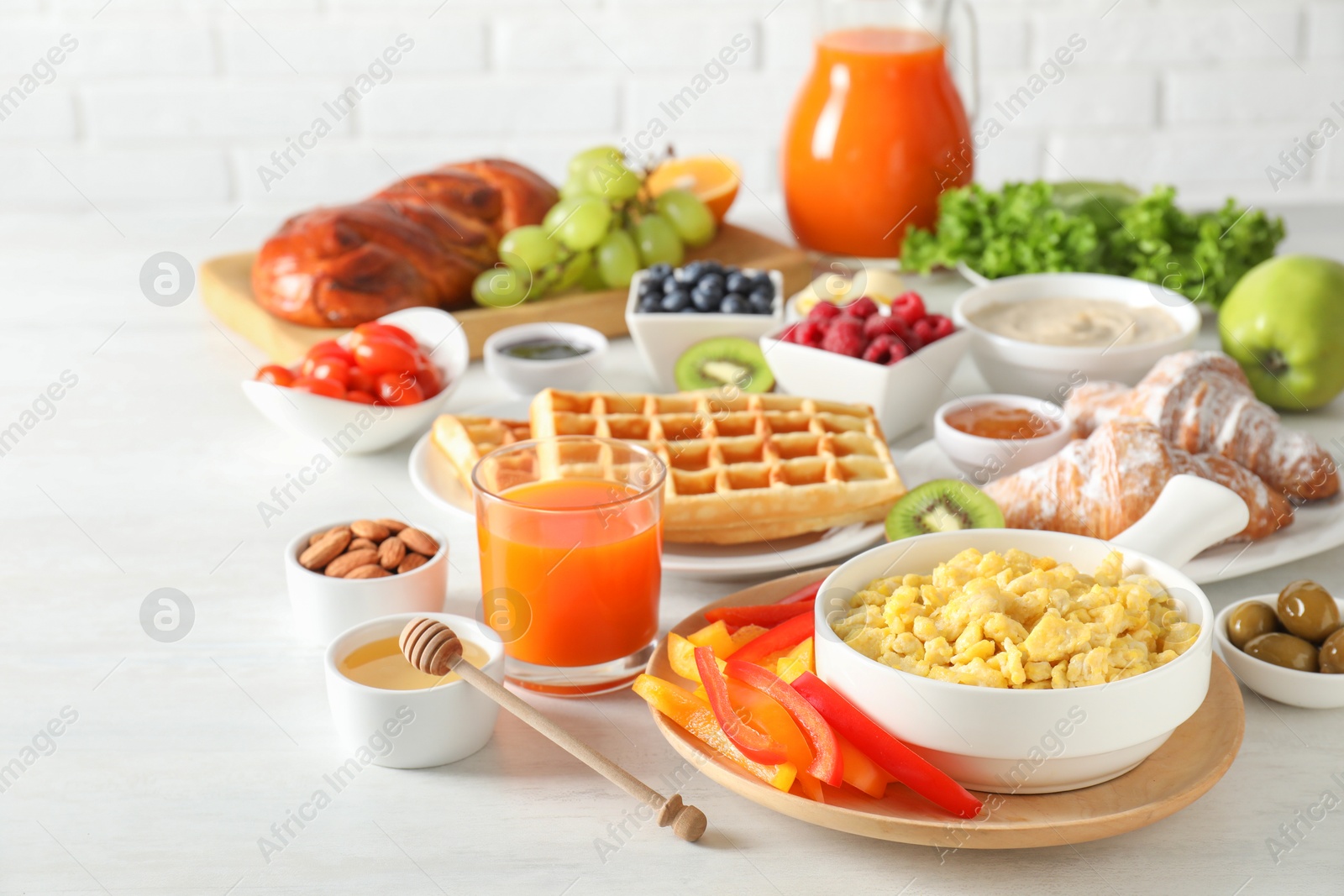 Photo of Tasty breakfast. Scrambled eggs in bowl, cut bell pepper, honey and other food on light table