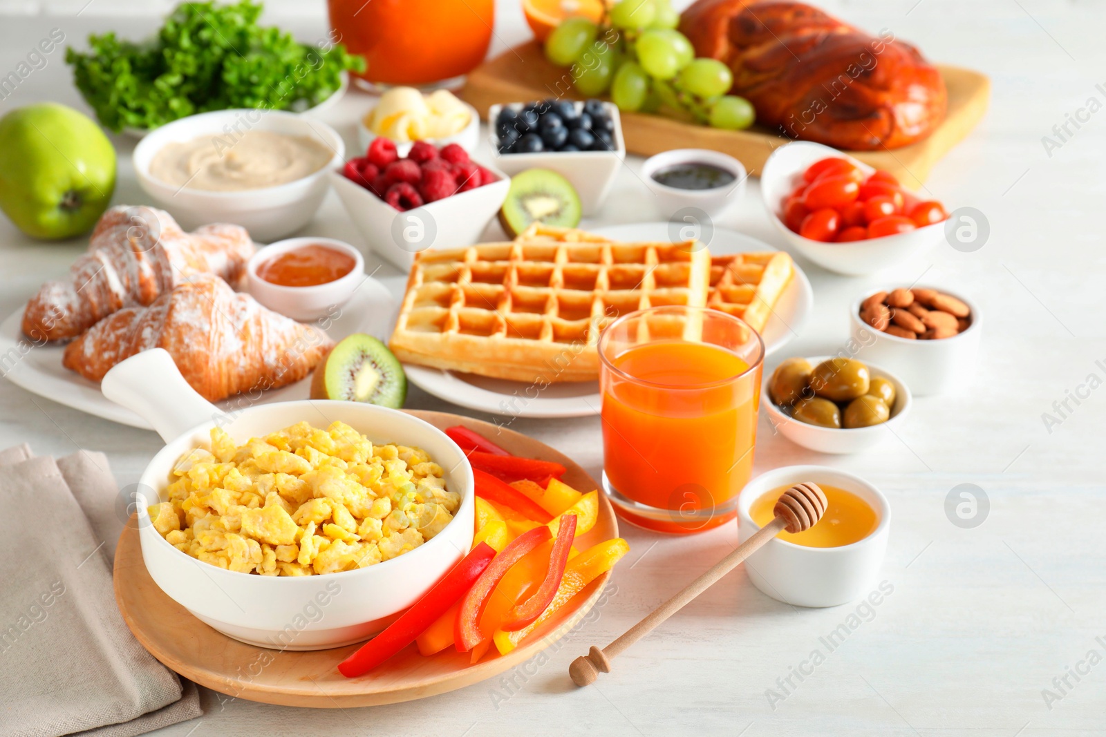 Photo of Tasty breakfast. Scrambled eggs in bowl, cut bell pepper, honey and other food on light table