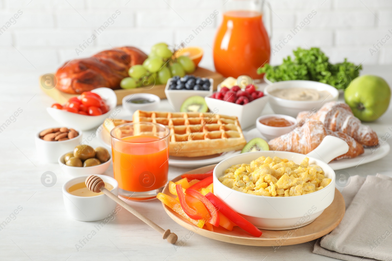 Photo of Tasty breakfast. Scrambled eggs in bowl, cut bell pepper, honey and other food on light table