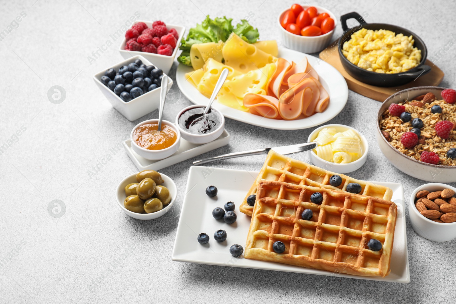 Photo of Tasty breakfast. Belgian waffles, blueberries and other food on grey textured table