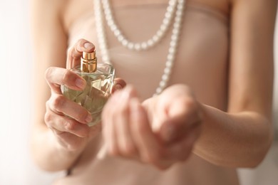 Photo of Woman spraying perfume onto wrist indoors, closeup