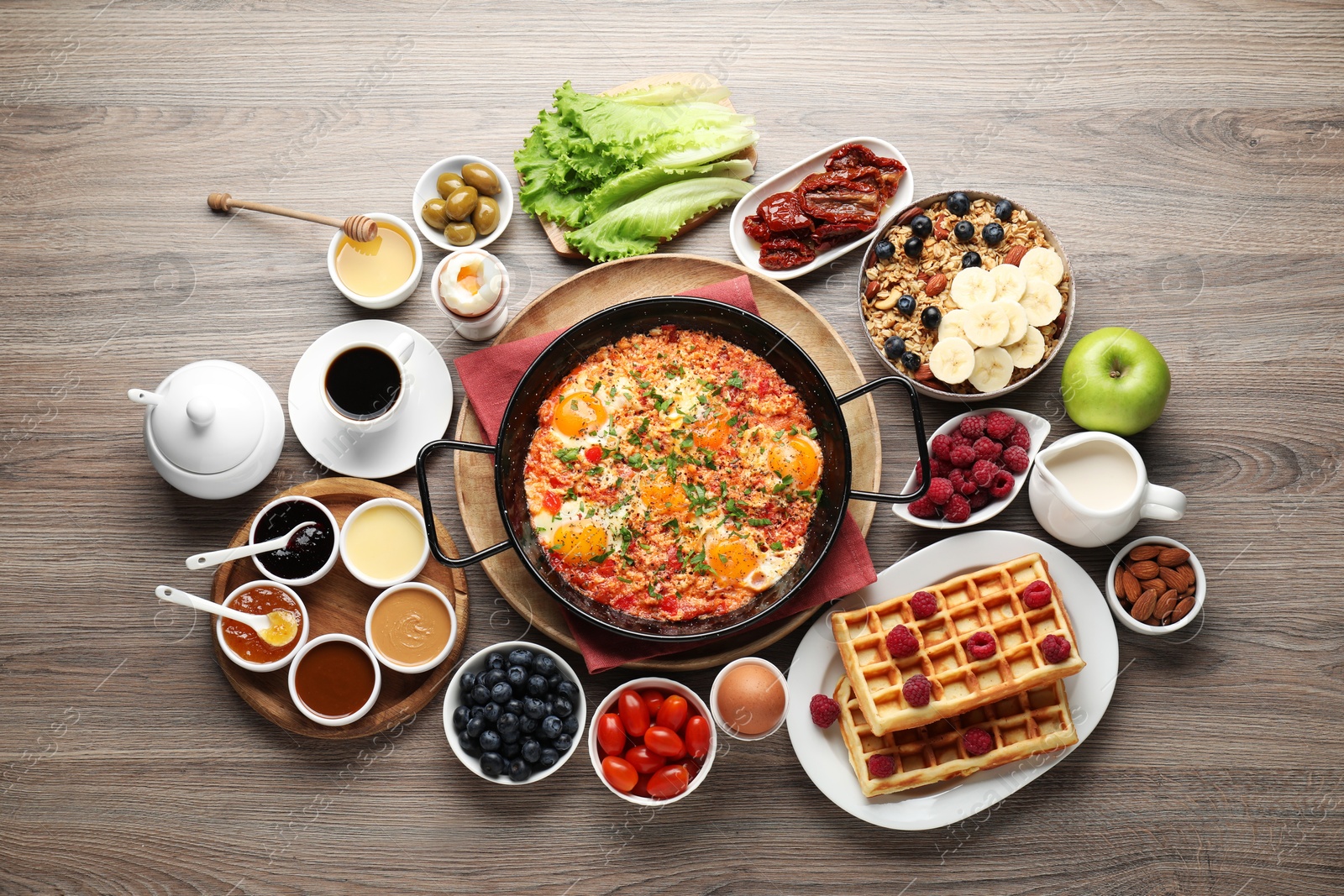 Photo of Tasty shakshouka in frying pan and other meals served for breakfast on wooden table, flat lay