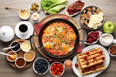 Photo of Tasty shakshouka in frying pan and other meals served for breakfast on wooden table, flat lay