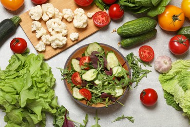 Photo of Healthy vegetarian food. Salad in bowl and vegetables on grey textured table, flat lay