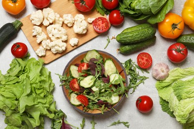 Photo of Healthy vegetarian food. Salad in bowl and vegetables on grey textured table, flat lay