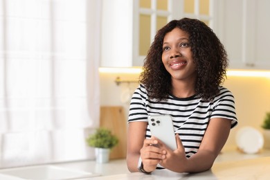 Photo of Beautiful woman with mobile phone at table indoors, space for text