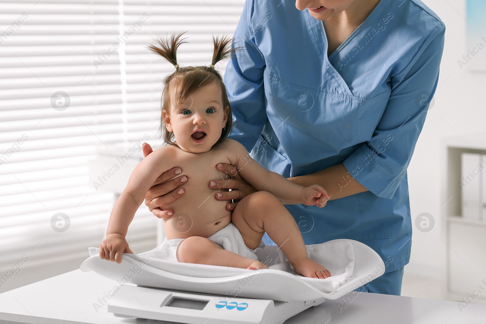 Photo of Pediatrician weighting cute little girl in clinic. Checking baby's health