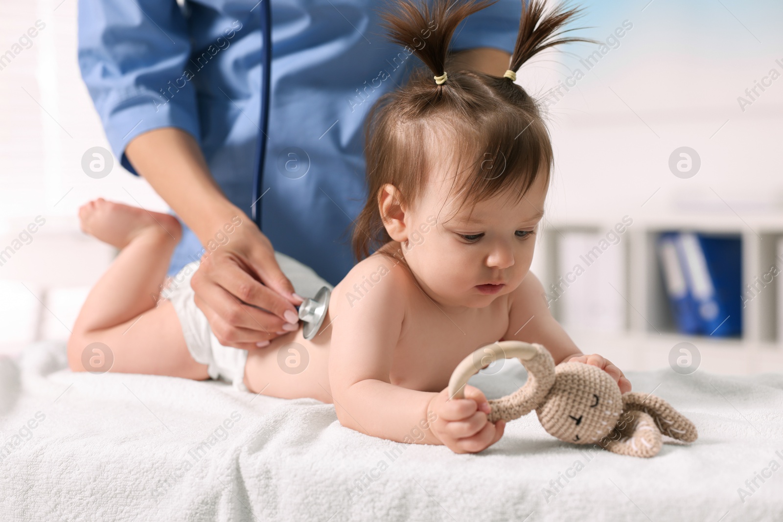 Photo of Pediatrician examining cute little girl with stethoscope in clinic, closeup. Checking baby's health