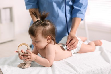 Photo of Pediatrician examining cute little girl with stethoscope in clinic, closeup. Checking baby's health