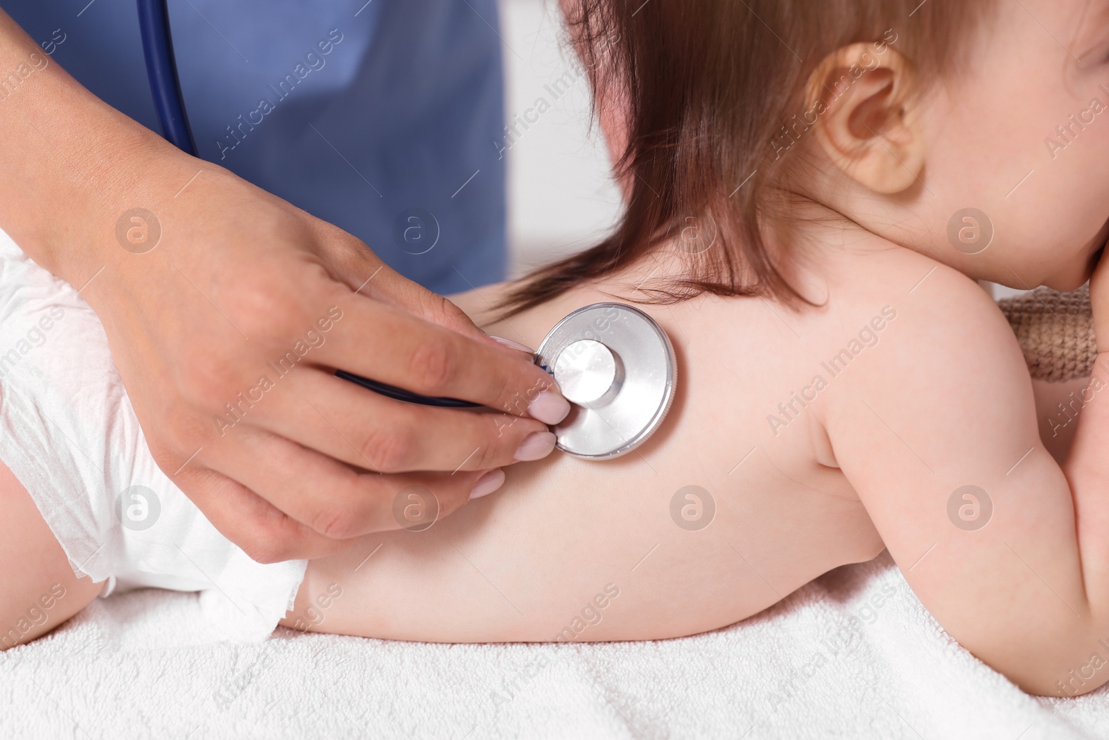 Photo of Pediatrician examining cute little girl with stethoscope in clinic, closeup. Checking baby's health