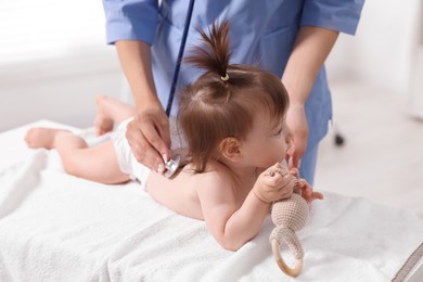 Pediatrician examining cute little girl with stethoscope in clinic, closeup. Checking baby's health