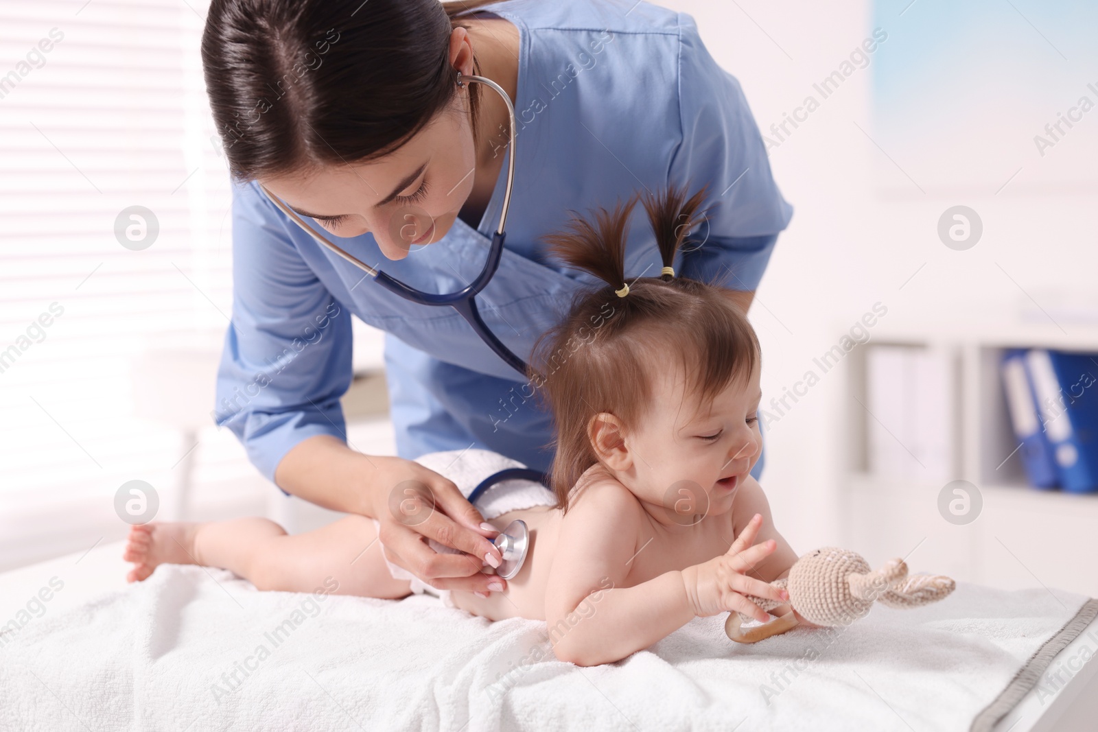 Photo of Pediatrician examining cute little girl with stethoscope in clinic. Checking baby's health