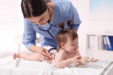 Photo of Pediatrician examining cute little girl with stethoscope in clinic. Checking baby's health