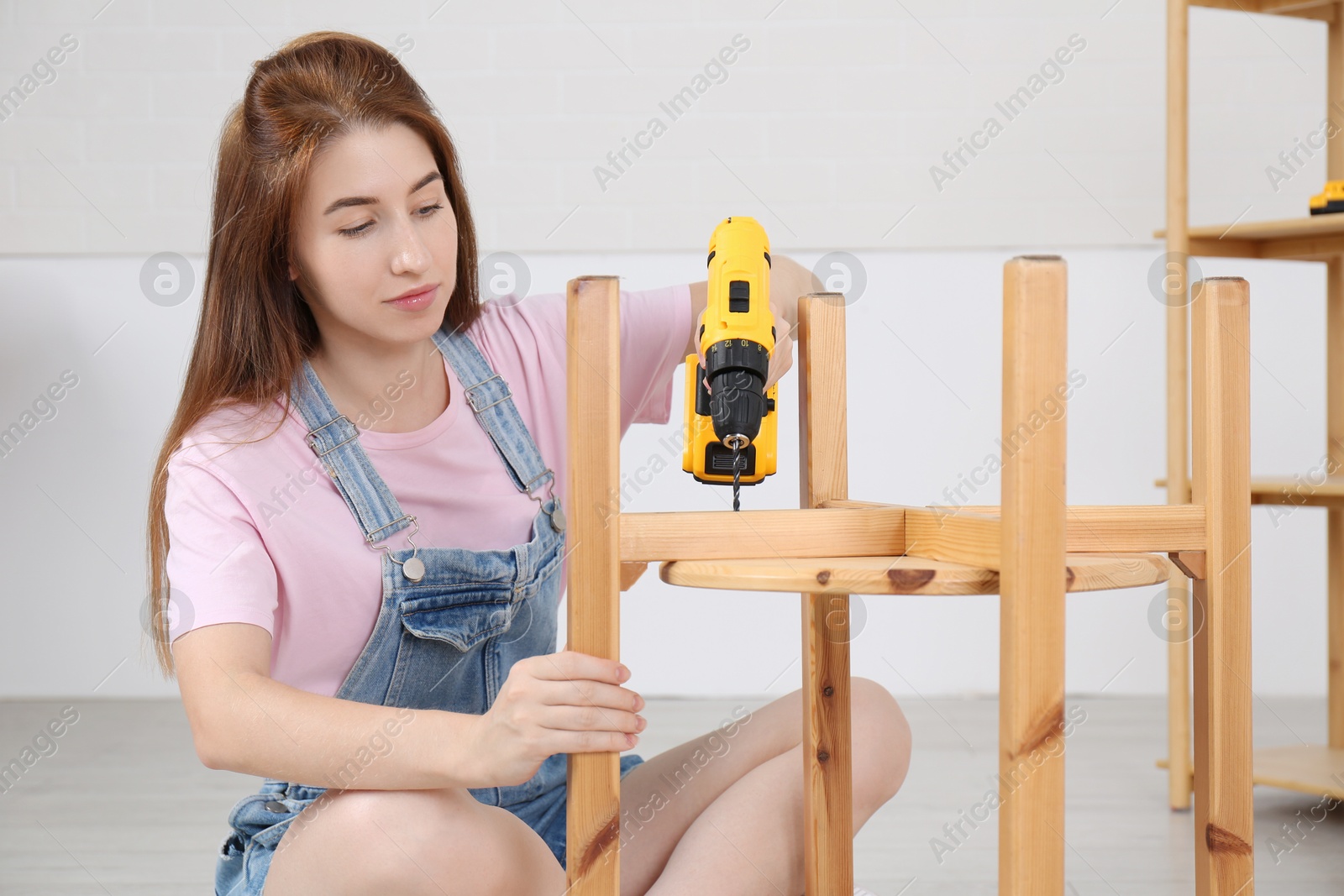 Photo of Woman with electric screwdriver assembling furniture indoors